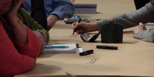 Menschen schreiben mit Stiften auf einer Tischdecke aus Papier