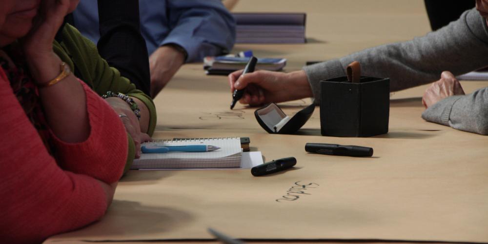 Menschen schreiben mit Stiften auf einer Tischdecke aus Papier