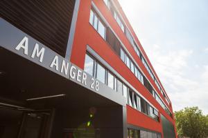 Eingangsbereich des Verwaltungsgebäudes Am Anger 28 mit roter Fassade vor blauem Himmel